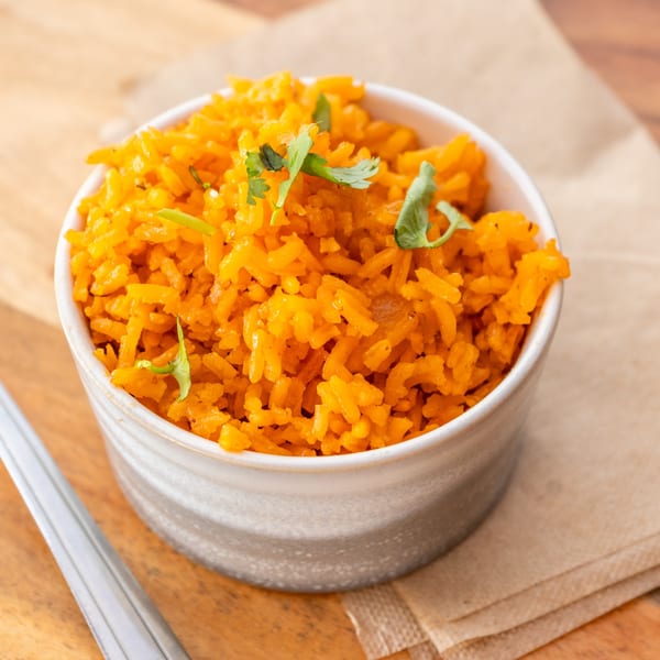 A white bowl filled with vibrant orange Mexican rice, garnished with fresh cilantro, on a wooden surface.