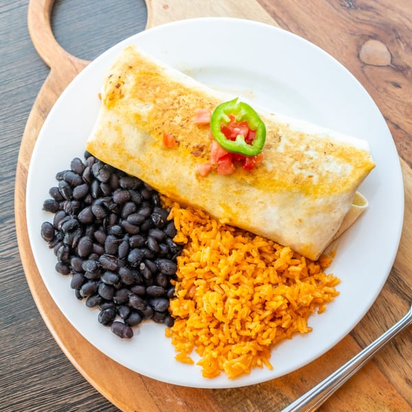 A golden-brown burrito topped with salsa and jalapeños, served with black beans and orange rice.