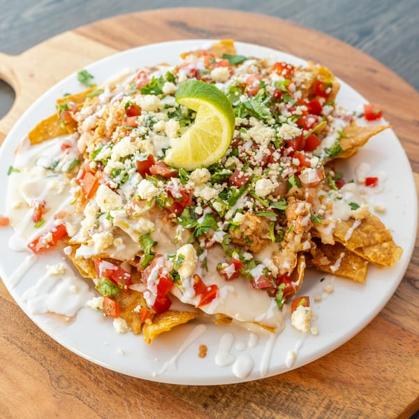 A plate of nachos with chicken, cheese, tomatoes, cilantro, and a lime wedge.