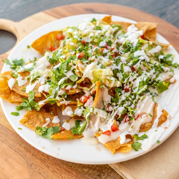 Crispy golden tortilla chips topped with fresh lettuce, tomatoes, cilantro, and creamy white sauce.