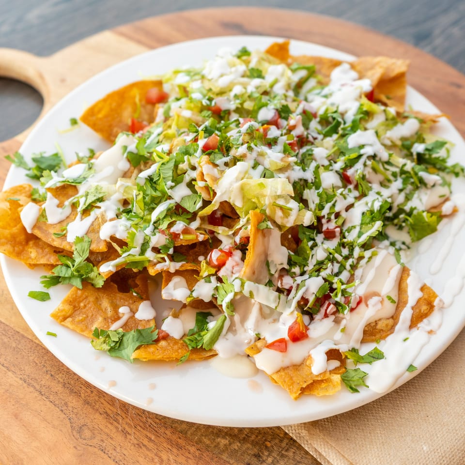 Crispy golden tortilla chips topped with fresh lettuce, tomatoes, cilantro, and creamy white sauce.