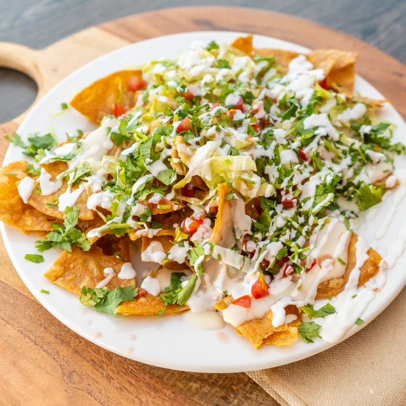 Crispy golden tortilla chips topped with fresh lettuce, tomatoes, cilantro, and creamy white sauce.